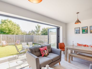 A living room with a gray sofa and dining table opening to a backyard with chairs and a table at Sea View in Llanfaelog