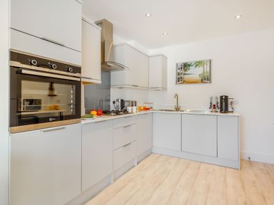 A modern kitchen with built in oven stove sink and coffee machine with a beach picture on the wall at Sea View in Llanfaelog