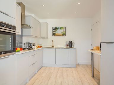 A kitchen with white cabinets and appliances including a stove oven refrigerator and coffee machine at Sea View in Llanfaelog