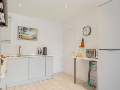 A kitchen with white cabinets a coffee machine a sink a microwave a loaf of bread and a door at Sea View in Llanfaelog