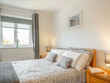 A bedroom with a bed with patterned bedding two bedside tables with lamps a window with curtains and a framed picture on the wall at Sea View in Llanfaelog