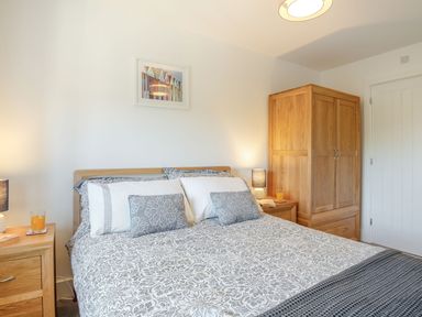 A bedroom with a double bed between two wooden nightstands and a wooden wardrobe in Sea View in Llanfaelog