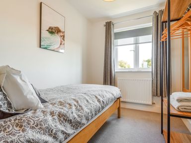 A bedroom with a single bed a window with curtains and a shelving unit with towels at Sea View in Llanfaelog