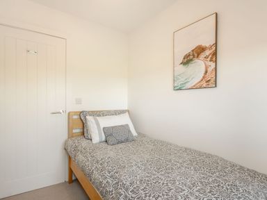 A bedroom with a single bed patterned bedding and a framed coastal picture on the wall at Sea View in Llanfaelog