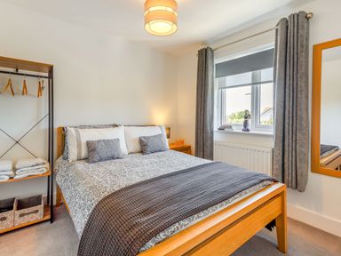A bedroom with a bed and patterned bedding next to a window with curtains and a standing clothes rack at Sea View in Llanfaelog