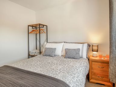 A bedroom with a bed two pillows a bedside table with a lamp two glasses and an open wardrobe with hangers and folded towels at Sea View in Llanfaelog