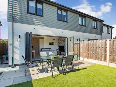 A garden patio with a glass table and four chairs outside a house with bi folding doors at Sea View in Llanfaelog