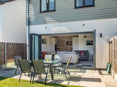A patio with a glass table and chairs opening into a living room with a sofa at Sea View in Llanfaelog