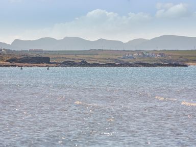 A coastal landscape with water in the foreground and houses and hills in the background at Sea View in Llanfaelog