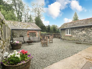An outdoor courtyard with wooden chairs tables stone walls and flower planters at Home Farmhouse Graythwaite near Hawkshead