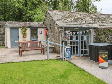 A small stone building with a shop entrance and bench outside at Home Farmhouse in Graythwaite near Hawkshead