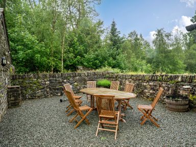 An outdoor dining area with a table and wooden chairs at Home Farmhouse at the Graythwaite Estate near Hawkshead