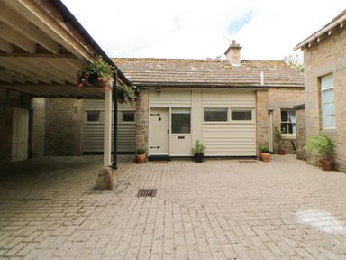 A cobblestone courtyard with potted plants around doorways and a covered parking area at The Coach House in Shepherd's Dene near Corbridge