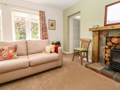 A living room with a beige sofa and floral cushions a wooden chair with a green cushion a fireplace with stacked logs and tiled hearth at The Coach House Shepherd's Dene near Corbridge
