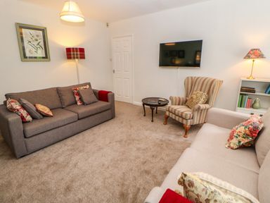A living room with two sofas an armchair a round table a wall mounted tv and a bookshelf at The Coach House Shepherd's Dene near Corbridge