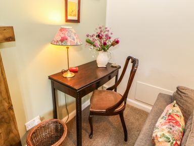 A wooden desk with a floral lamp and vase of flowers next to a wooden chair and a grey sofa with a floral cushion at The Coach House in Shepherd's Dene near Corbridge