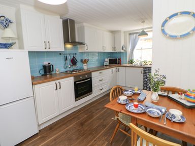 A kitchen with white cabinets blue tile backsplash and a wooden dining table set with blue and white dishes at The Coach House Shepherd's Dene near Corbridge