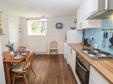 A kitchen with wooden flooring a dining table set with plates and cups a window and white cabinets at The Coach House Shepherd's Dene near Corbridge