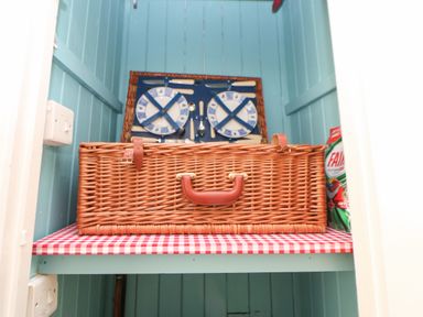 A picnic basket with plates and cutlery on a shelf with a red and white checkered liner at The Coach House Shepherd's Dene near Corbridge