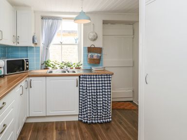 A kitchen with white cabinets blue tiled backsplash wooden counters and a blue and white check curtain at The Coach House in Shepherd's Dene near Corbridge