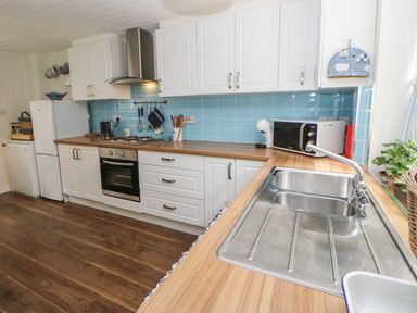 A kitchen with white cabinets wooden countertops a stainless steel sink a microwave oven and a refrigerator at The Coach House Shepherd's Dene near Corbridge