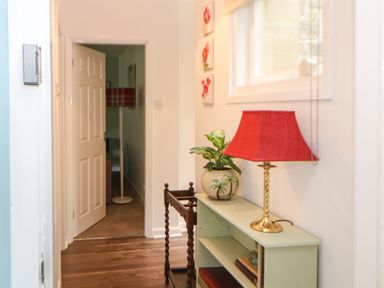 A hallway with a green bookcase holding a lamp and a plant next to an open doorway at The Coach House Shepherd's Dene near Corbridge