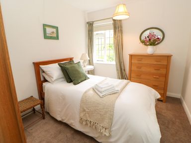 A bedroom with a single bed white bedding green pillows a wooden chest of drawers and window at The Coach House in Shepherd's Dene near Corbridge