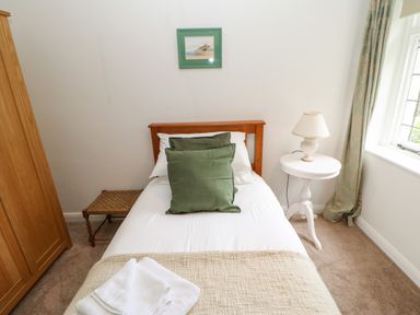 A bedroom with a single bed with green pillows a wooden wardrobe a white round bedside table with a lamp and a window with curtains at The Coach House in Shepherd's Dene near Corbridge