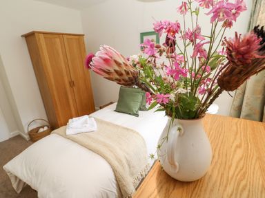 A bedroom with a single bed with white linens and green pillows next to a wooden wardrobe and a bouquet of flowers in a ceramic jug on a wooden table at The Coach House Shepherd's Dene near Corbridge