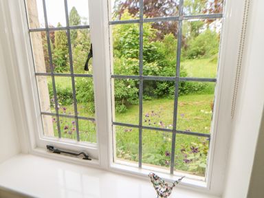 A window with metal grid bars looking out to a garden with greenery and purple flowers at The Coach House Shepherds Dene near Corbridge