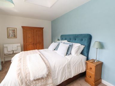 A bedroom with a bed with pillows and a blanket a wooden wardrobe a bedside table with a lamp and a towel rack at The Coach House Shepherd's Dene near Corbridge