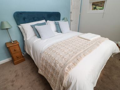 A bedroom with a bed with white bedding and blue pillows a wooden nightstand with a lamp and a window at The Coach House Shepherd's Dene near Corbridge