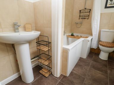 A bathroom with a sink and storage rack a bathtub with shower and wooden shelf and a toilet with wooden seat at The Coach House in Shepherds Dene near Corbridge