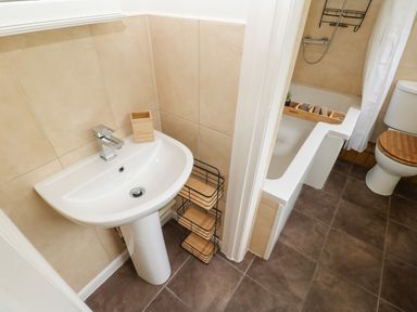 A bathroom with a pedestal sink and faucet next to a bathtub with a wooden tray and a toilet with a wooden seat at The Coach House in Shepherd's Dene near Corbridge