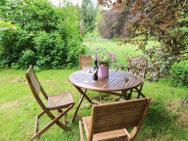 A wooden outdoor table with four chairs on grass surrounded by bushes and trees at The Coach House in Shepherd's Dene near Corbridge