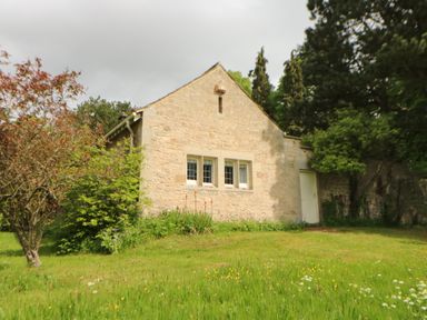 A stone building with three windows and a door surrounded by grass and trees at The Coach House in Shepherd's Dene near Corbridge