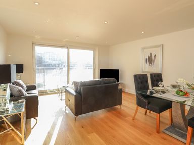 A living room with black sofas glass dining table and sliding doors at Harbourside Haven Apartment 2 in Weymouth