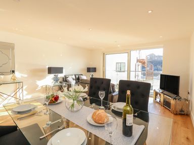 A dining area with a glass table set for four and a living room with sofas and a television at Harbourside Haven Apartment 2 in Weymouth