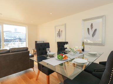 A dining table with plates glasses a bowl of vegetables and flowers next to a living area with sofas and framed feather artwork at Harbourside Haven Apartment 2 in Weymouth