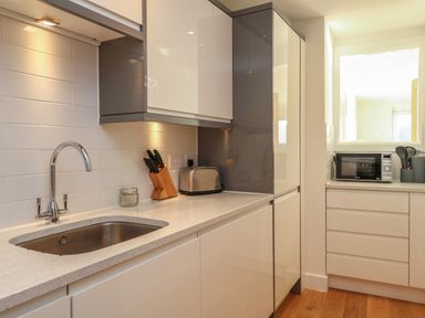 A kitchen with a sink a faucet knives in a holder a toaster and a microwave at Harbourside Haven Apartment 2 in Weymouth