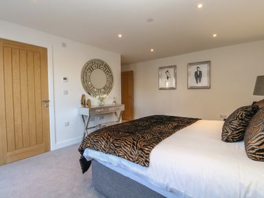 A bedroom with a bed, a console table with decorative items, a round mirror, and two framed pictures at Harbourside Haven Apartment 2 in Weymouth
