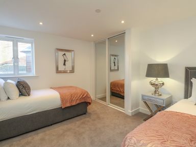 A bedroom with two single beds a bedside table with a lamp a window and mirrored wardrobe doors at Harbourside Haven Apartment 2 in Weymouth
