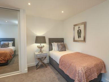 A bedroom with a single bed a side table with a lamp a framed picture and a mirrored wardrobe at Harbourside Haven Apartment 2 in Weymouth