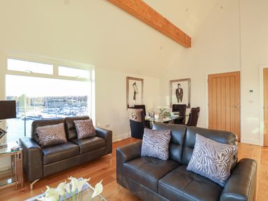 A living room with leather sofas and a dining table by a window overlooking boats at Harbourside Haven Penthouse 1 in Weymouth