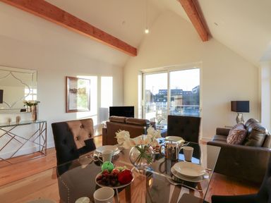 A dining and living area with glass table chairs sofas and a large window at Harbourside Haven Penthouse 1 in Weymouth