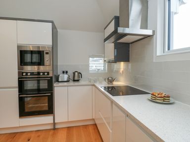 A kitchen with white cabinets a built-in oven microwave toaster kettle cooktop and a plate of muffins at Harbourside Haven Penthouse 1 in Weymouth