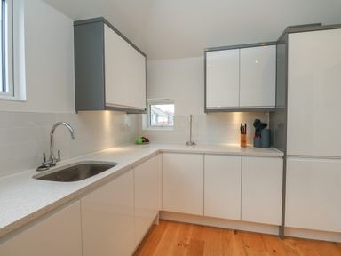 A kitchen with white cabinets a stainless steel sink a countertop with kitchen utensils and a window at Harbourside Haven Penthouse 1 in Weymouth