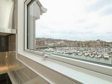 A kitchen window overlooking a marina with boats and buildings at Harbourside Haven Penthouse 1 in Weymouth