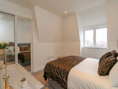 A bedroom with a bed covered in patterned throws and pillows near a window and mirrored closet doors at Harbourside Haven Penthouse 1 in Weymouth