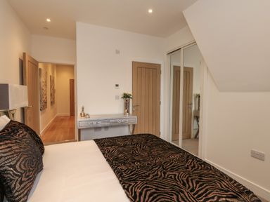 A bedroom with a bed covered in patterned bedding a wooden door a mirrored closet door and a small silver table with flowers at Harbourside Haven Penthouse 1 in Weymouth